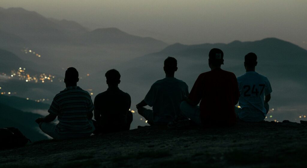 Five people sit on a hilltop overlooking a distant city