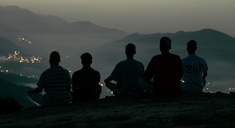 Five people sit on a hilltop overlooking a distant city