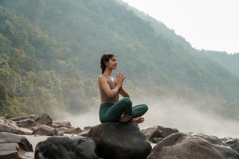 a woman sitting on top of a rock next to a river